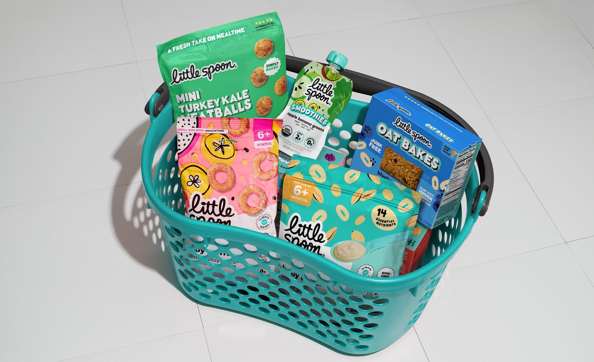Shopping basket filled with Little Spoon products, including Mini Turkey Kale Meatballs, a Smoothies pouch, Oat Bakes, and snacks.